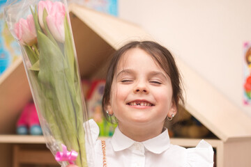 Little girl with a bouquet of pink tulips on the background of toothless smiling looking at the...