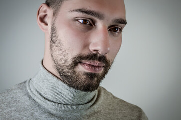 Portrait of a young brown-haired man with a short beard and a gray turtleneck sweater	