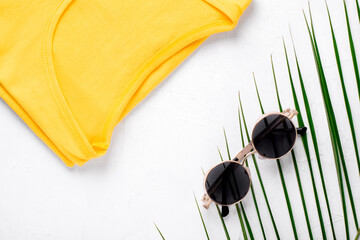 Round sunglasses, palm leaf and yellow T-shirt on white. Summer fashion flat lay
