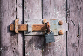 Old metal padlock on a closed no entry, closed bolted and barred old wooden door.