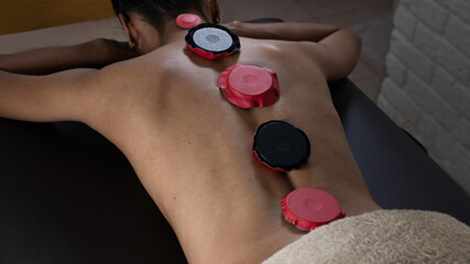 Brunette woman lying on a therapeutic stretcher with biomagnetism therapy magnets placed on her...