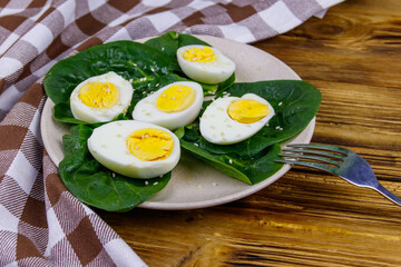 Boiled eggs with fresh spinach leaves and sesame seeds on wooden table