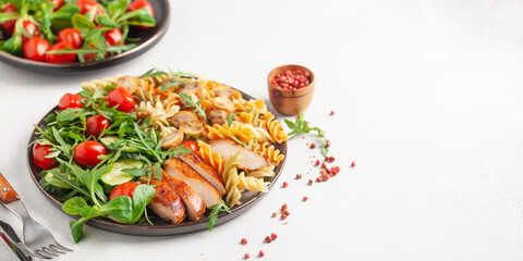 Grilled chicken breast, pasta fusilli, arugula, tomatoes, cucumber slice and mushrooms  in plate.