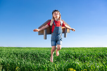 Happy child jumping against blue sky. Kid having fun in spring green field outdoor
