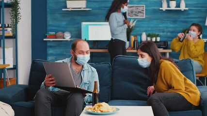 Group of friends planning project using laptop spending weekend together in living room wearing protective masks and respecting social distancing against spreading covid19 virus in global pandemic