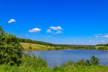 Summer landscape with beautiful lake, green meadows, hills, trees and blue sky