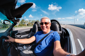 Fisheye view of a handsome middle age man driving a convertible automobile on the highway