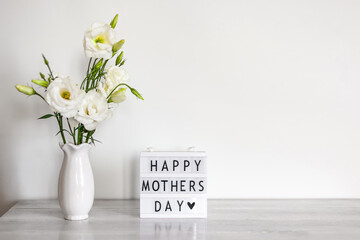 Light box with lettering Happy Mother's Day, white flowers Eustoma or Lisianthus in vase on white wooden table with copy space