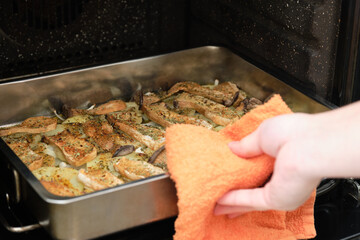 Cropped image of man hands taking a tray with seasoned sliced king trumpet mushrooms (pleurotus eryngii), potatoes and onions from oven. Mediterranean diet.
