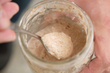 Close up of hands with a spoon grabbing part of sourdough starter. Fermented culture to prepare bread.