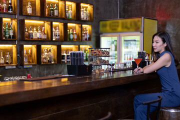 Young Asian woman with a sad face drinking cocktails in front of a vintage bar, Relaxing activities after work or hangouts, Place of entertainment for young adolescents or night club party.