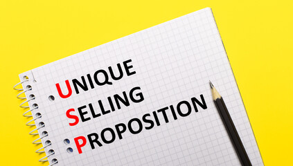 Obraz premium White notebook with inscription USP Unique Selling Proposition written in black pencil on a bright yellow background.