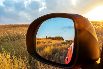 Reflected field and forest in rearview mirror at sunset. Concept of car eco travel around your country, travel to future or past, ways to change