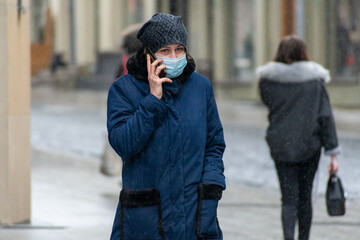 Girl or woman walking with mask and talking on the phone in the street under the rain during Covid or Coronavirus emergency