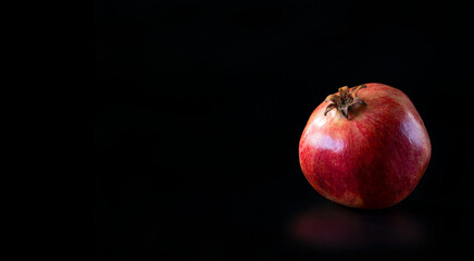 Fototapeta na wymiar Ripe red pomegranate fruit close-up sunbeam black background horizontal image free space to text summer healthy diet vitamins