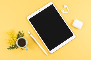 Tablet with earphones and pencil on yellow background. Copy space.