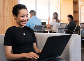 Fototapeta premium african american woman working and typing in laptop on sofa in office lobby. .
