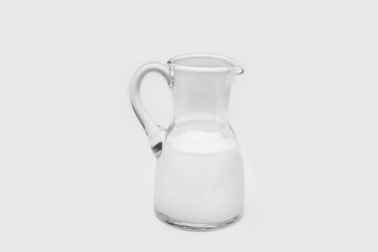 Glass pitcher half full with milk on a white background
