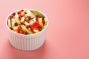 Salad of different juicy ripe fruits in a white cup on a pink background.