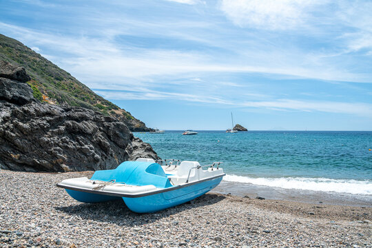 Tretboot am Strand ohne Personen mit Felsen und Booten im Hintergrund