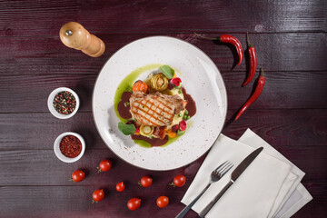 Pork with grilled vegetables, red wine sauce, olive oil on a white plate on a wooden table. View from above.