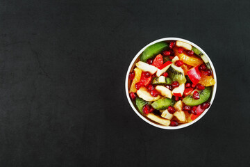 Fruit salad in a white cup on a black background, free space for text.