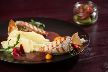 Grilled chicken fillet with mashed potatoes, sauce on the background of a jar of salad on a wooden table.