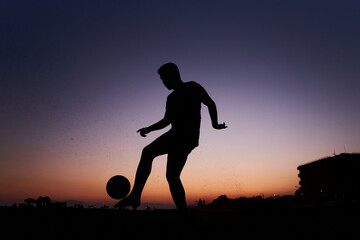 Silhouette of young man playing soccer on the beach with a ball at sunset