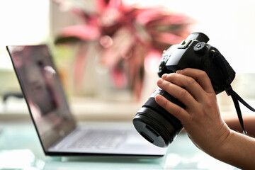 The camera in a man's hand against the background of a laptop turned on. Selective focus.