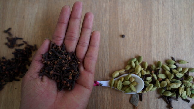 A man holding cardamom pods and cloves in his palm. Indian organic spices on Kitchen background. Indian veg spice.