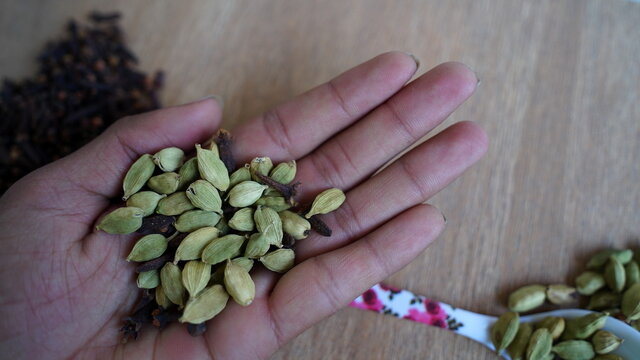 A man holding cardamom pods and cloves in his palm. Indian organic spices on Kitchen background. Indian veg spice.