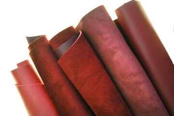Genuine leather isolated on white background.Red and burgundy genuine leather in rolls close-up on...