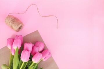 Pink tulips in craft paper on pink background. Florist preparing bouquet of fresh beautiful tulips. Easter, Valentine's Day, Mother's day. Spring card. Place for text. Minimalism