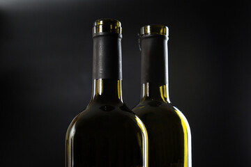 two open bottles of wine stand side by side on a dark glossy background.