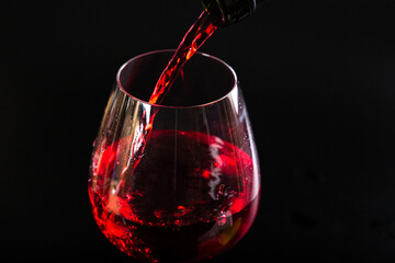 Naklejka na ściany i meble Pouring red wine with splashes and drops into a glass on a black background.