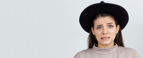 Indoor shot of cute girl looking at the camera, having doubtful and indecisive face expression,...