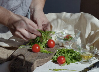 In the kitchen, a woman's hands prepare a light vegetable salad on a wooden board from arugula, tomato and olia
