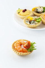 Tartlet with shrimp, tomato and greens on the background of a plate with tartlets.