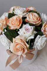 Artificial roses in a round box on a white table, close-up. Decorative bouquet of flowers.