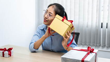 Young asian woman holding a presents box while sitting at office workspace