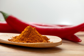 A few pods of red hot pepper and a wooden spoon with seasoning on a brown wooden background.