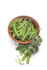 Pods of green peas with leaves in bowl isolated on white background
