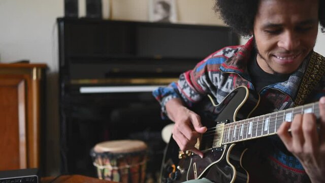 Afro man musician playing guitar at in living room