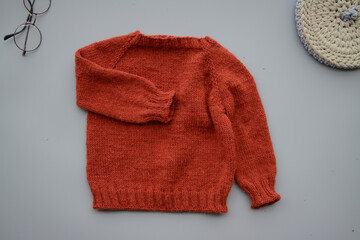 Red woolen handmade baby sweater on gray background