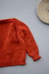 Red woolen handmade baby sweater on gray background