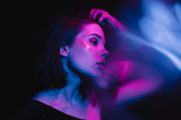 Stylish gentle portrait of a young woman in trendy makeup with glitter on a dark background posing...