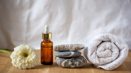 Dark glass vessel with essential oil cosmetic product for skin care, massage and spa at home. Stack of stones, hand towel and white flower on the wooden towel and white flower on the wooden table. 