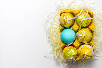 Dnipro, Ukraine - April 07, 2020: Painted and colored eggs in yellow paper egg tray isolated on white background. Easter creative idea. Top view, close-up, copy space