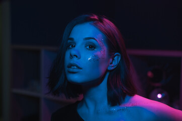 Portrait of an attractive woman in makeup with glitter posing indoors in blue and purple light....
