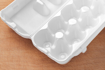 White styrofoam egg packaging. Wooden table with fine texture. The food item lies and casts a soft shadow.